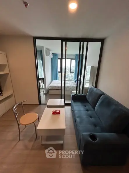 Modern living room with blue sofa and view into bedroom through glass doors.