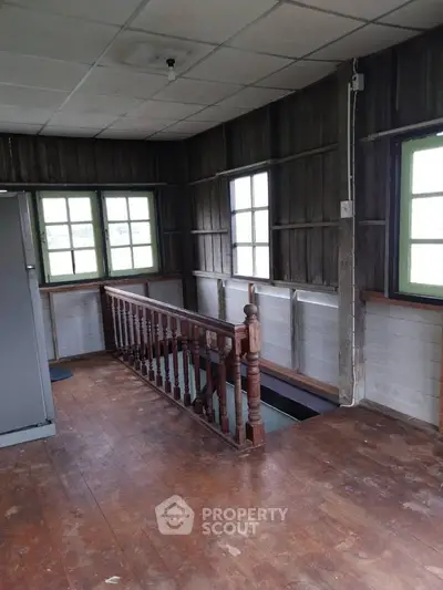 Charming rustic interior with wooden floors and staircase, featuring large windows for natural light.