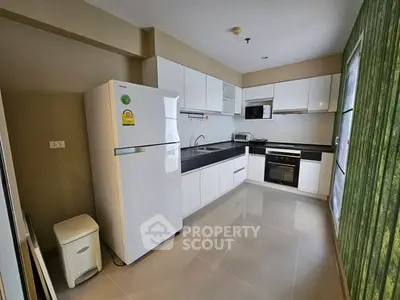 Modern kitchen with sleek white cabinets, fridge, and built-in oven in a bright apartment.