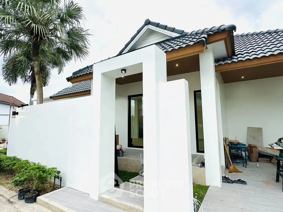 Modern single-story house with sleek white exterior and tiled roof, featuring a stylish entrance and lush greenery.