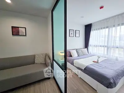 Modern studio apartment with cozy living area and stylish bedroom separated by glass partition.