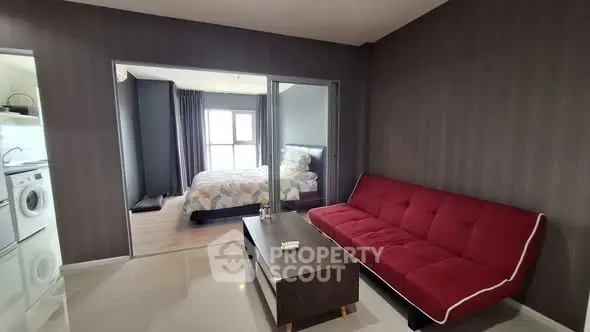 Modern apartment interior with red sofa and view into cozy bedroom