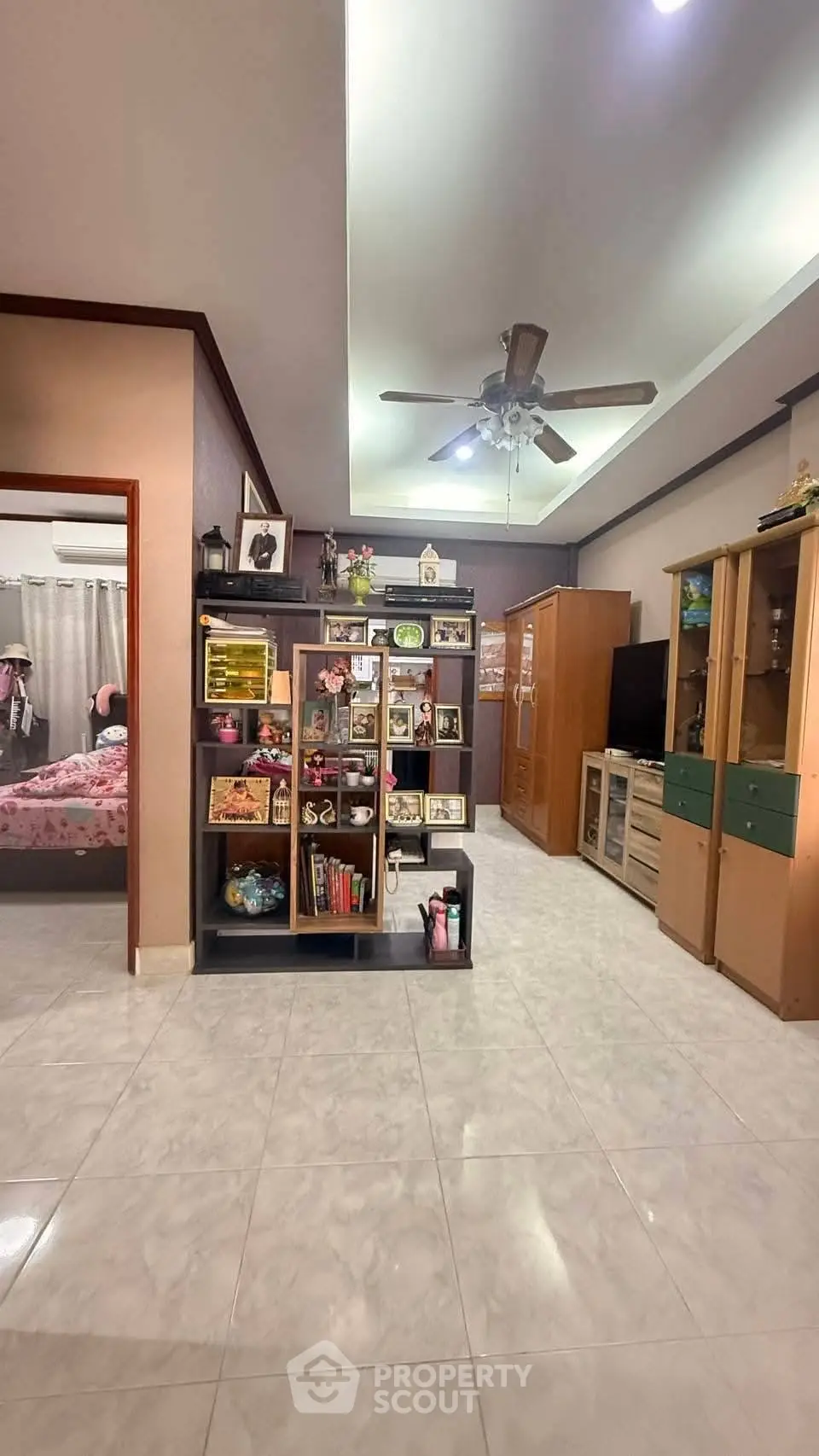 Spacious living area with ceiling fan and open shelving, leading to a cozy bedroom.