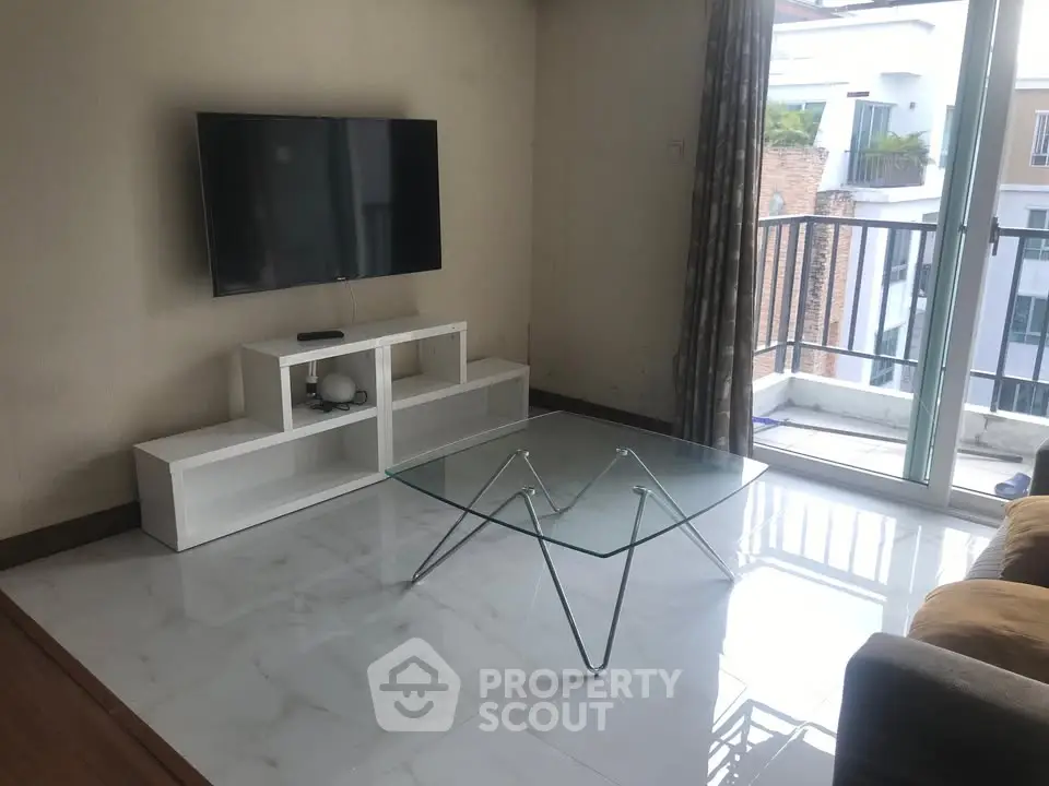 Modern living room with glass coffee table and wall-mounted TV, featuring a balcony view.