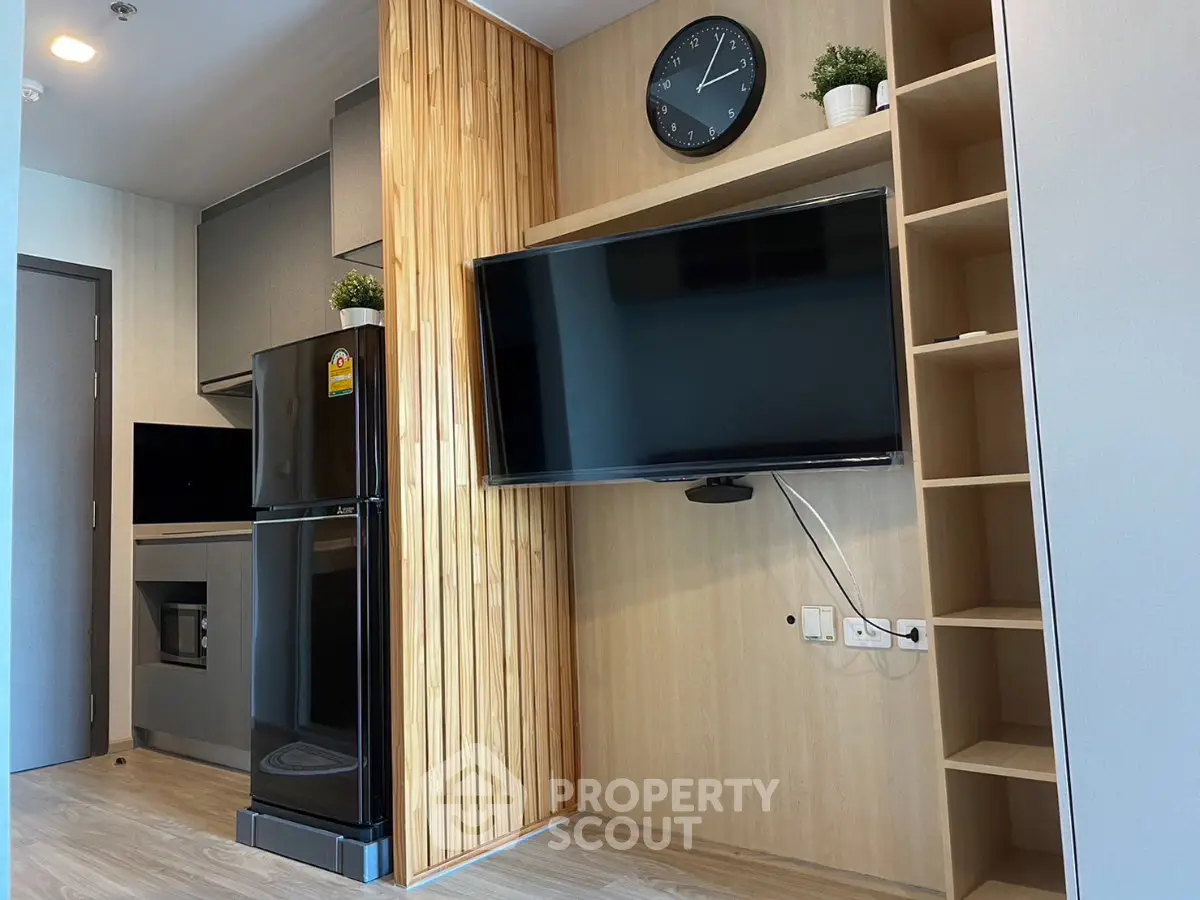 Modern living room with sleek TV, stylish shelving, and compact kitchen area.