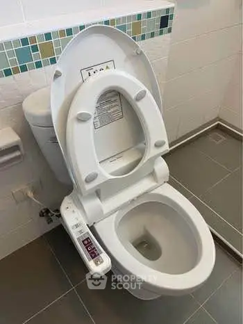 Modern bathroom with high-tech toilet featuring bidet controls and sleek tile design.