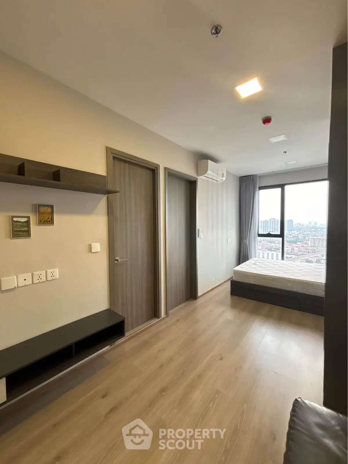 Modern bedroom with large window offering city view, featuring sleek wooden flooring and minimalist design.