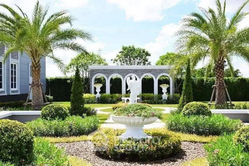 Luxurious garden with palm trees and elegant statues in a serene real estate setting.