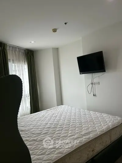 Cozy bedroom with natural light and wall-mounted TV in modern apartment.