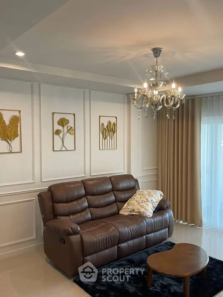 Elegant living room with leather sofa, chandelier, and stylish wall decor.