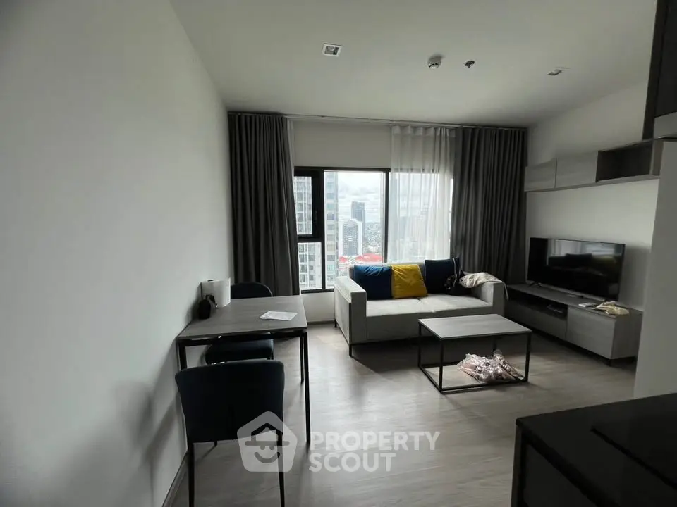 Modern living room with sleek furniture and large window offering city views.