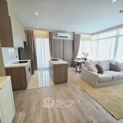 Modern open-layout living room with kitchen, featuring sleek design and ample natural light.
