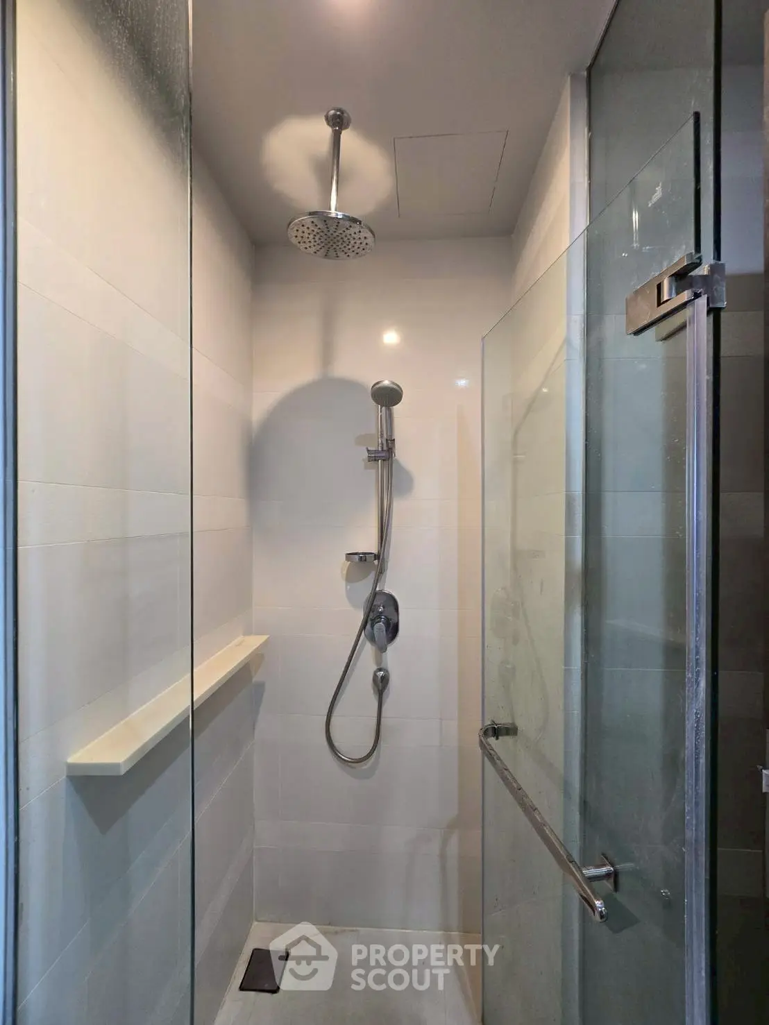 Modern shower area with glass door and rainfall showerhead in sleek bathroom.