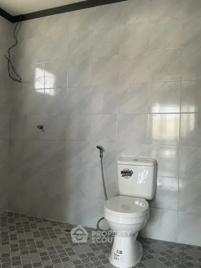 Modern bathroom with tiled walls and floor featuring a toilet and bidet spray.