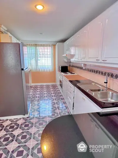 Spacious modern kitchen with sleek black countertops and stylish geometric floor tiles.