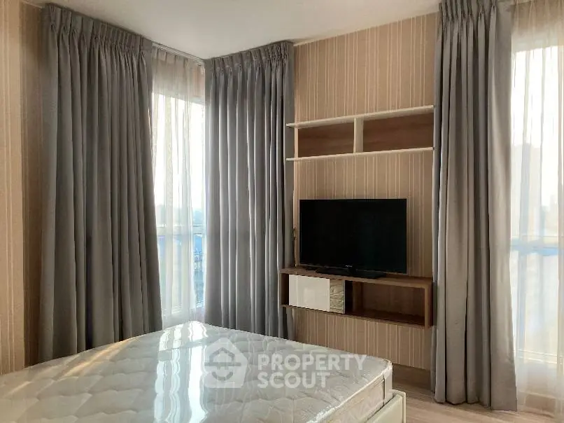 Modern bedroom with large windows and wall-mounted TV, featuring elegant curtains and a comfortable mattress.