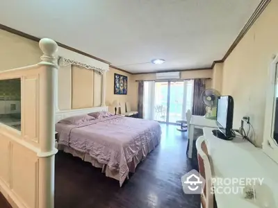 Spacious bedroom with polished hardwood floors, large bed, and abundant natural light streaming through glass doors leading to a balcony.