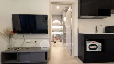 Modern living room with wall-mounted TV and sleek kitchen area in open layout apartment.