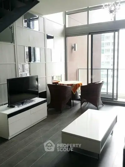 Modern living room with large windows and balcony access, featuring sleek furniture and natural light.