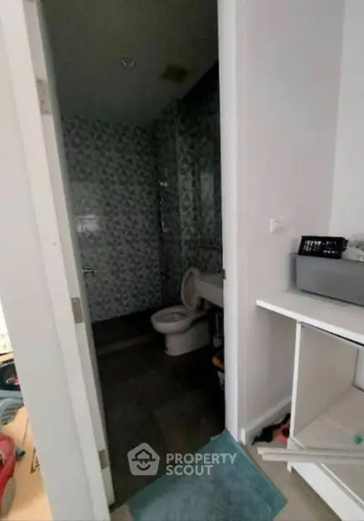 Compact bathroom with modern design and tiled walls, featuring a toilet and storage space.