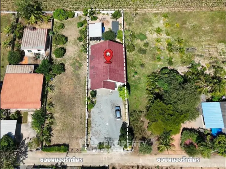 Aerial view of a property with a house, driveway, and surrounding greenery, ideal for real estate investment.