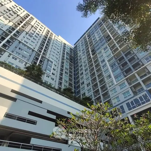 Modern high-rise building with lush greenery and clear blue sky.