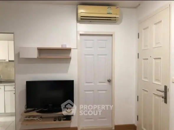 Modern apartment interior with TV, air conditioning, and kitchen view.