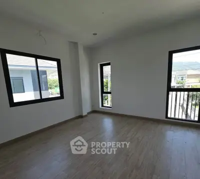 Bright empty room with large windows and wooden flooring, offering a serene view of the neighborhood.