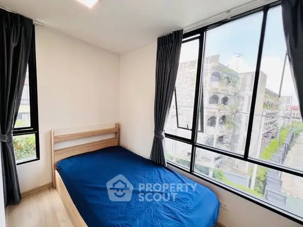 Bright bedroom with large windows and blue bedding, offering a city view.