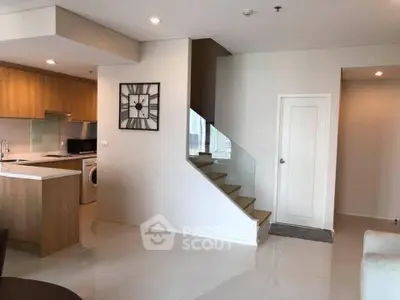 Modern open-plan living area with kitchen and staircase, featuring sleek design and natural light.