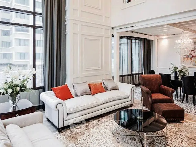 Luxurious living room with high ceilings, elegant decor, and large windows offering city views.
