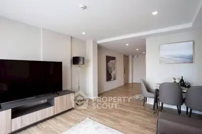 Modern living room with sleek decor and dining area, featuring a large flat-screen TV and elegant furnishings.