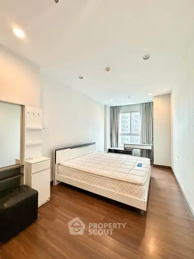 Spacious bedroom with large window and modern furnishings in a high-rise apartment.