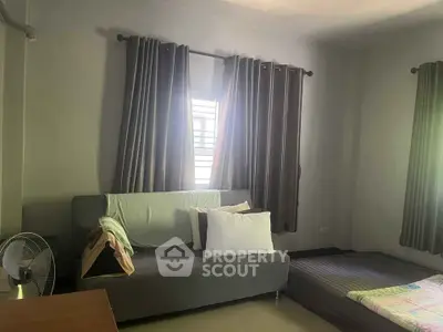 Cozy bedroom with sofa and bed, featuring natural light and elegant curtains.
