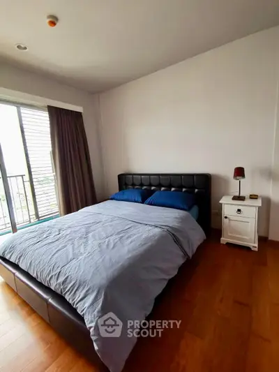 Spacious bedroom with modern bed and natural light from balcony window.