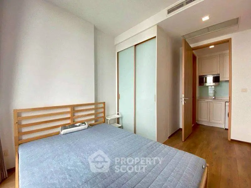 Modern bedroom with wooden flooring and sliding closet doors, adjacent to a compact kitchen.