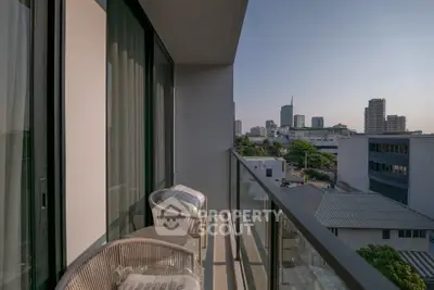 Modern balcony with city view, glass railing, and cozy seating area in urban apartment.