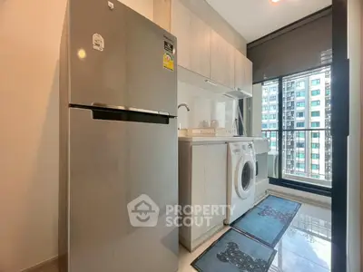 Modern kitchen with stainless steel fridge and washing machine, bright window view.