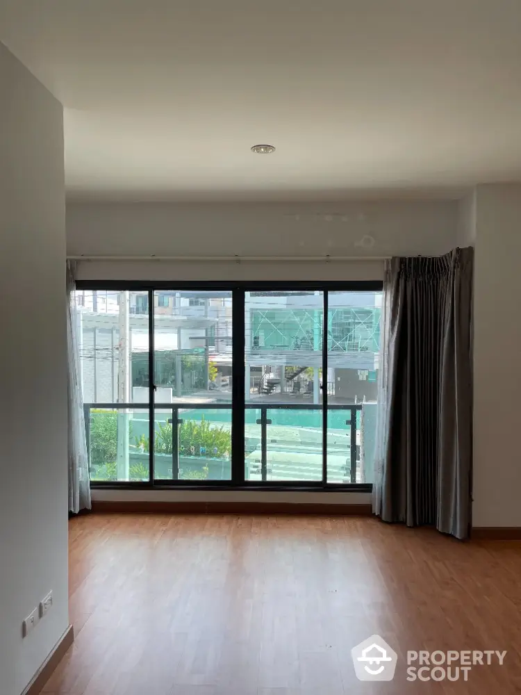 Spacious living room with large windows and wooden flooring, offering a bright and airy ambiance.