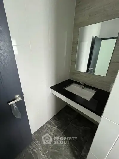 Modern bathroom with sleek black countertop and large mirror in contemporary apartment.