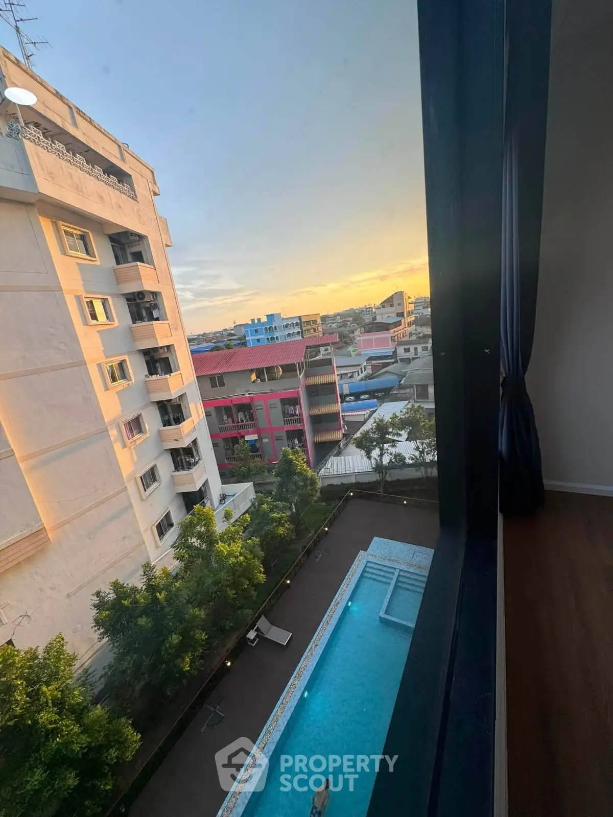 Stunning sunset view from high-rise apartment overlooking pool and cityscape.