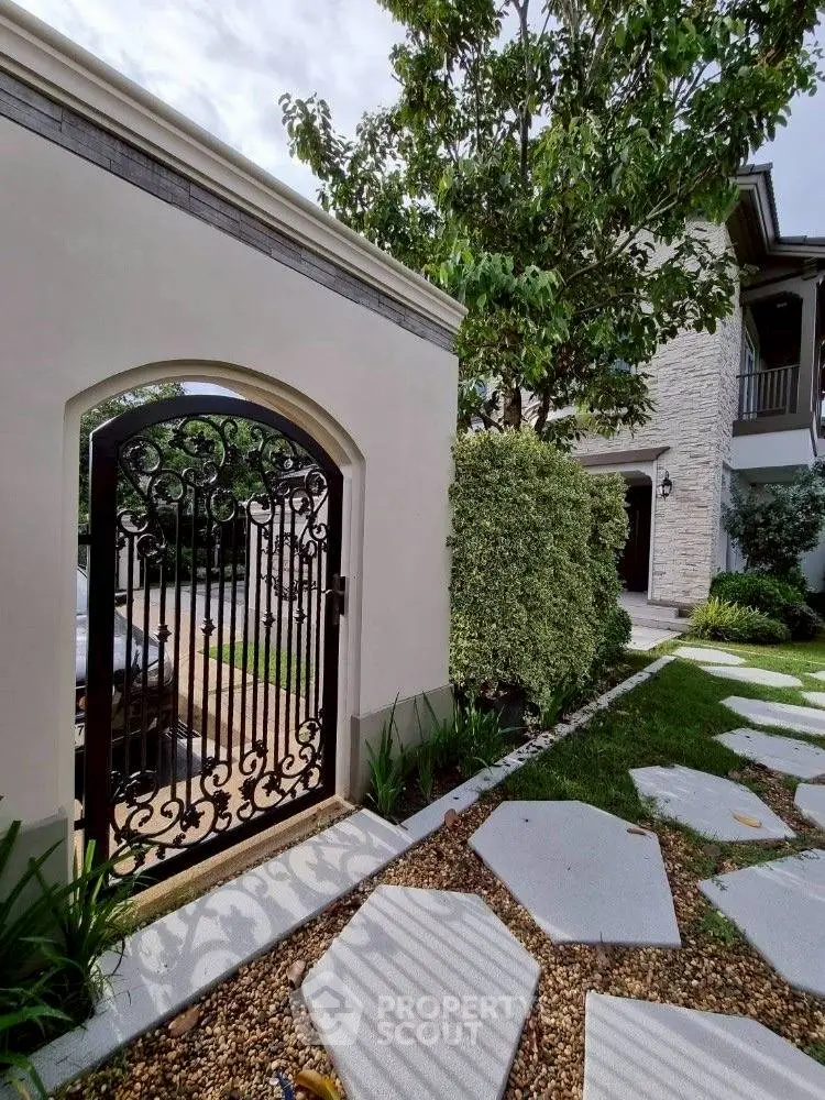 Charming garden entrance with elegant wrought iron gate and lush greenery.