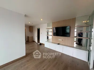 Spacious modern living room with sleek wooden flooring and mounted TV, perfect for entertainment.