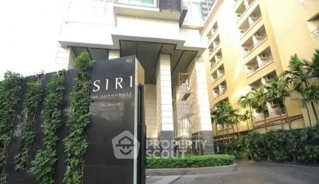 Modern condominium entrance with lush greenery and sleek architectural design.