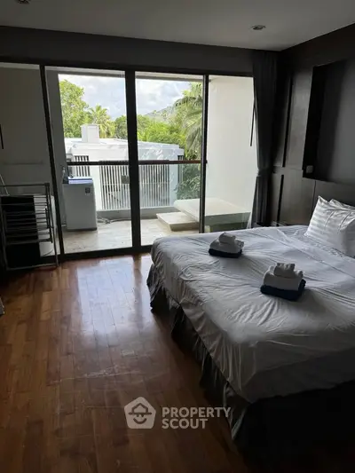 Spacious bedroom with balcony and scenic view, featuring modern decor and wooden flooring.