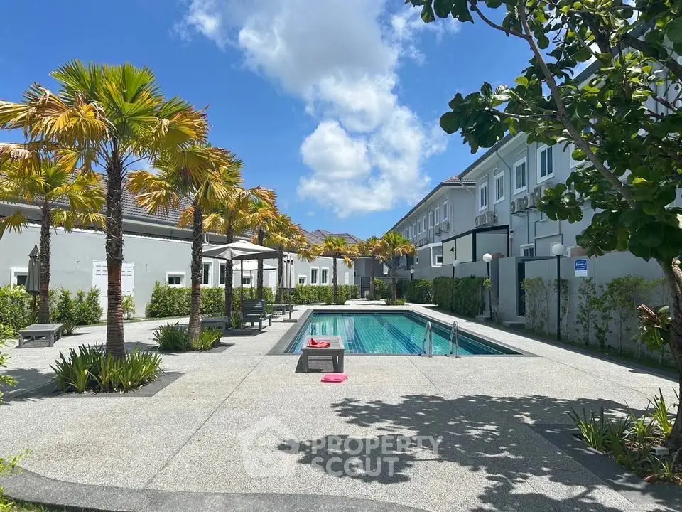 Luxurious residential pool area with palm trees and modern architecture under a clear blue sky.