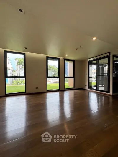 Spacious living room with large windows and wooden flooring, offering a bright and airy ambiance.