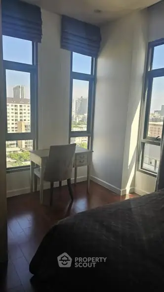 Bright bedroom with large windows offering stunning city views, featuring a cozy study nook.