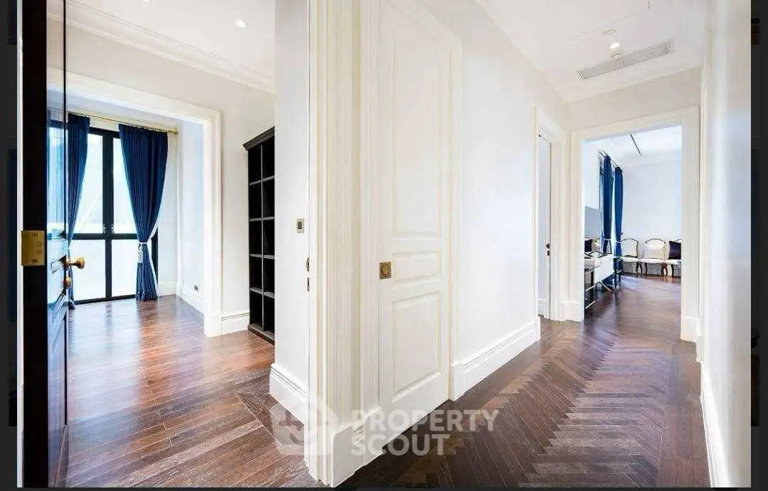 Elegant hallway with wooden flooring and bright natural light, leading to spacious rooms with stylish decor.
