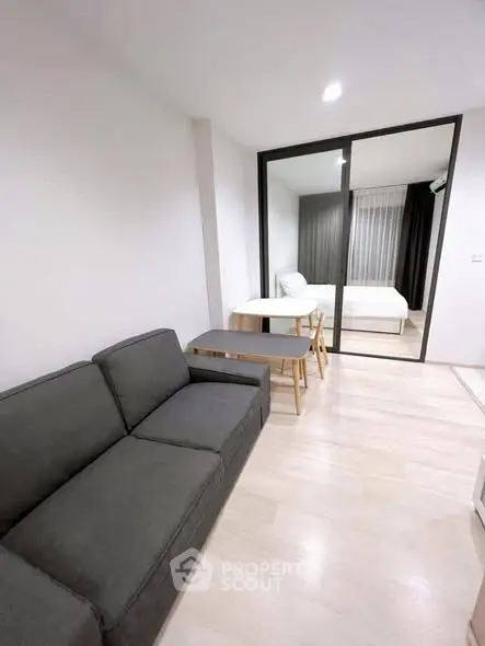 Modern apartment interior with cozy living room and bedroom separated by glass sliding doors.